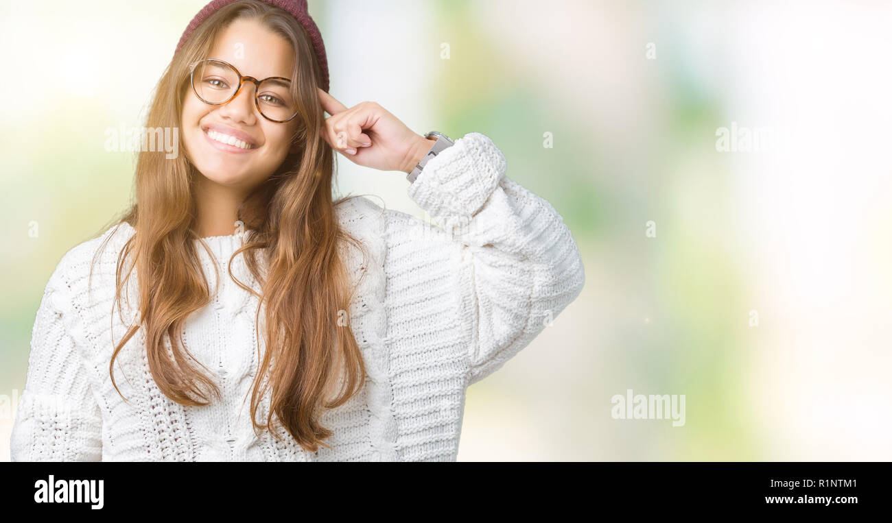 Young beautiful brunette hipster woman wearing glasses and winter hat over isolated background Smiling pointing to head with one finger, great idea or Stock Photo
