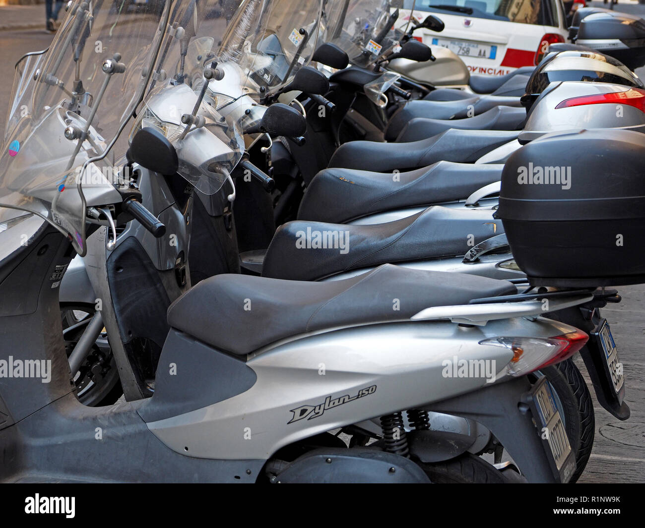 row of 7 almost identical silver Vespa or Honda motor scooters parallel parked in a street in central Florence,Tuscany,Italy Stock Photo