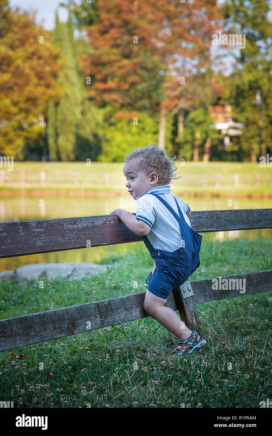 Happy little kid having fun climbing on the fence in park on warm summer day Stock Photo