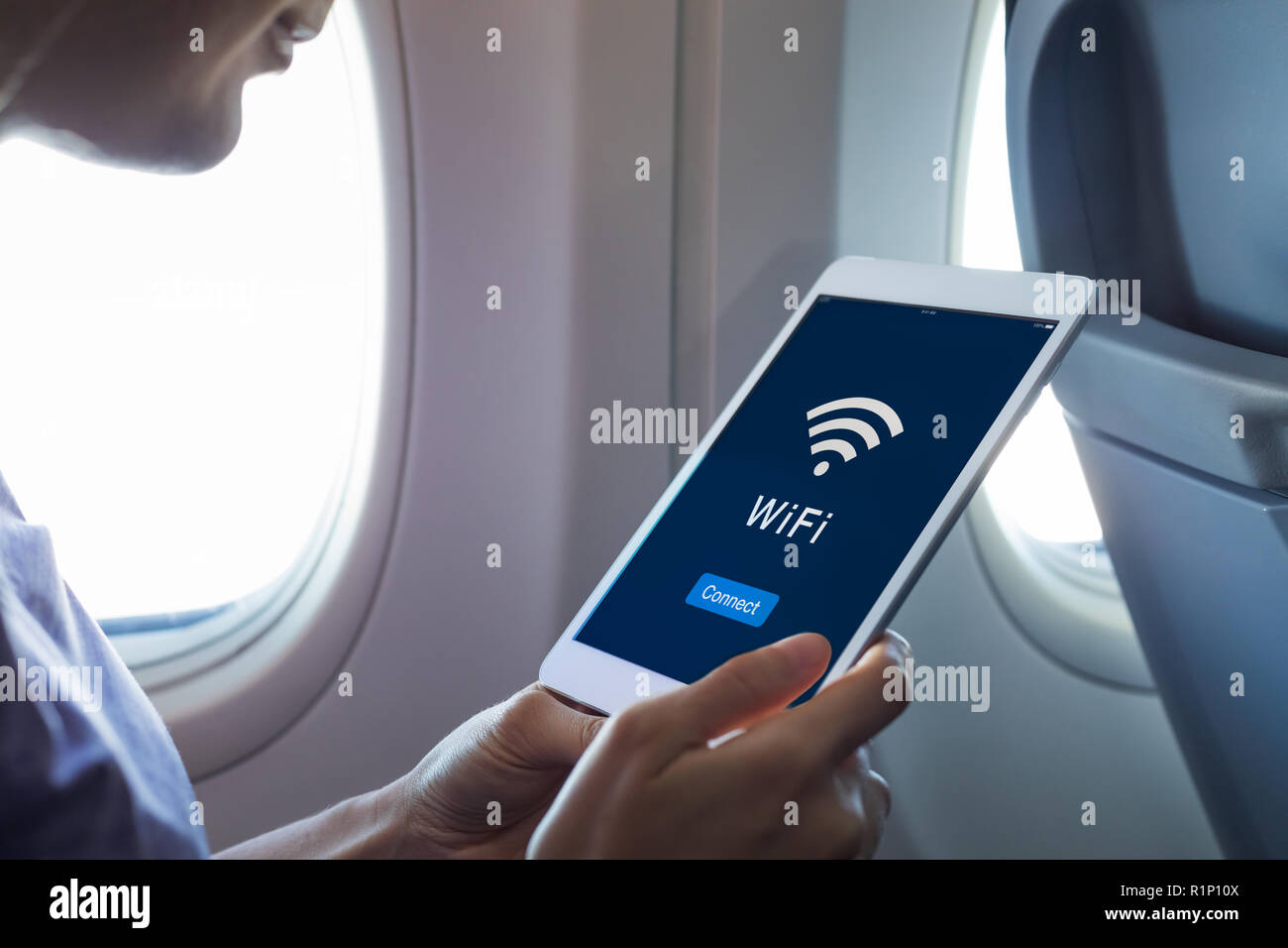 Wifi internet access in airplane during flight, passenger using tablet computer to connect to wireless network technology onboard to read email while  Stock Photo