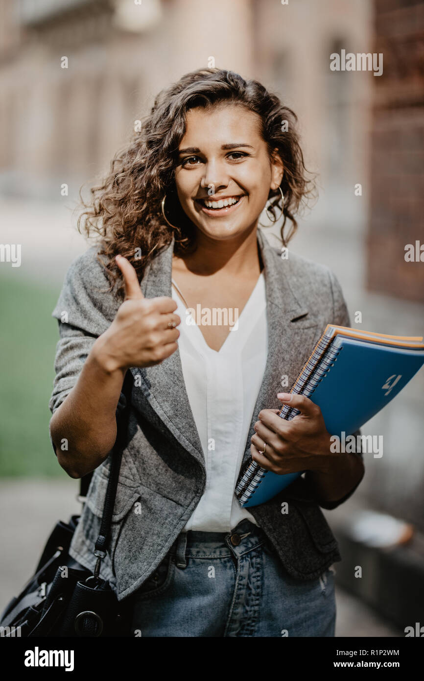 Portrait of a smiling female student showing thumb up outdoors Stock ...