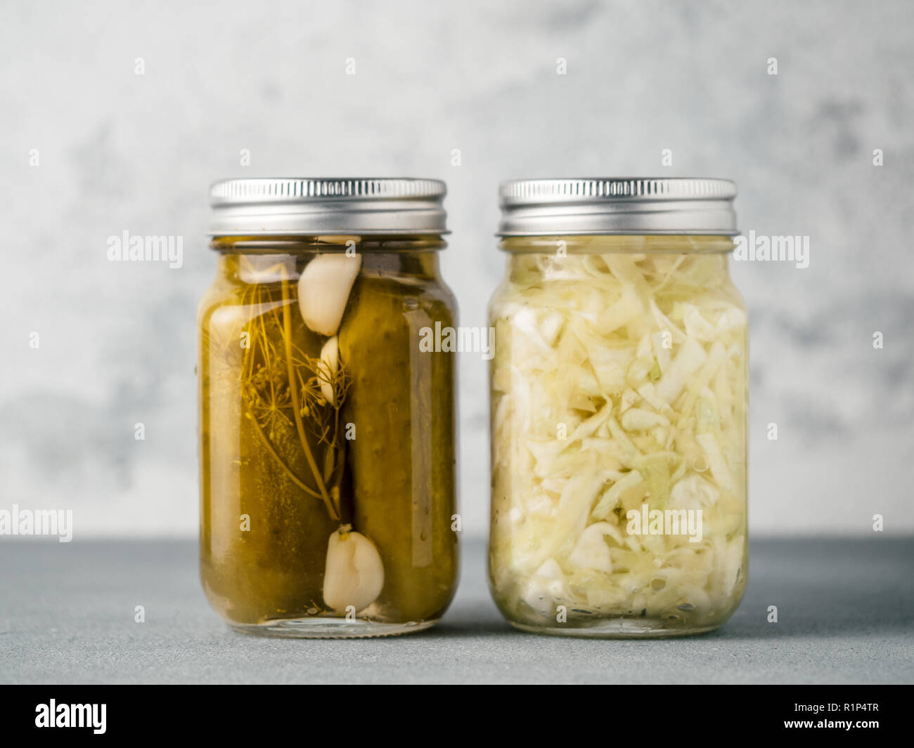 Pickled cucumbers and Sauerkraut on gray background. Perfect homemade marinated cucumbers and pickling cabbage in mason jar at home on table. Stock Photo