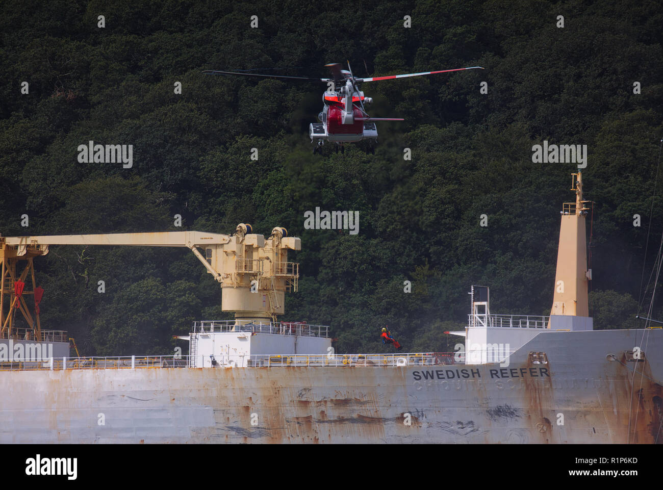 Coastguard helicopter hovering above the tanker and a helicopter crew member being winched down to help the casualty. River Fal, Cornwall. Stock Photo