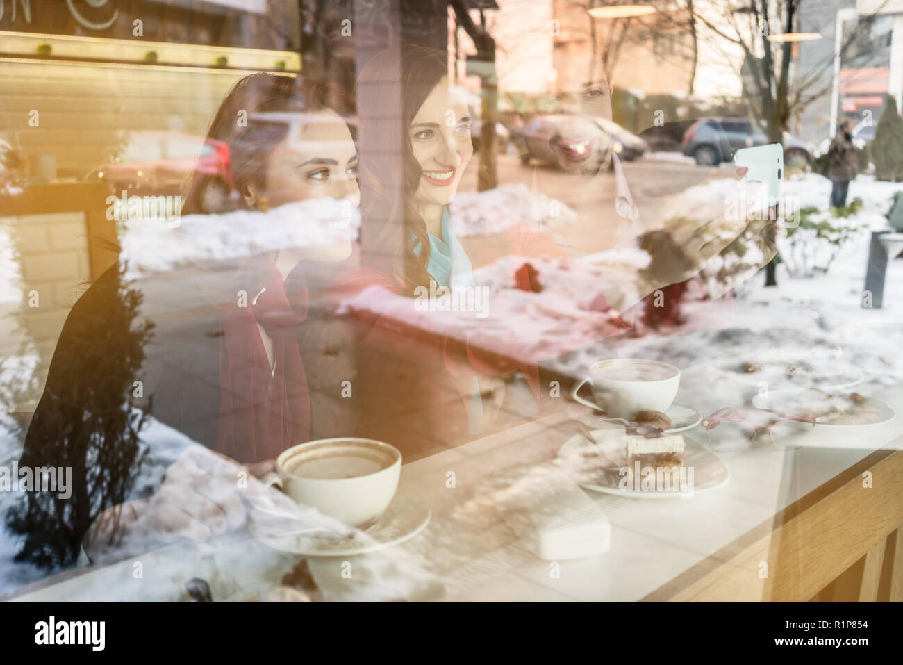 Two young cheerful women and best friends sharing a selfie picture on social media while relaxing together in a trendy coffee shop Stock Photo