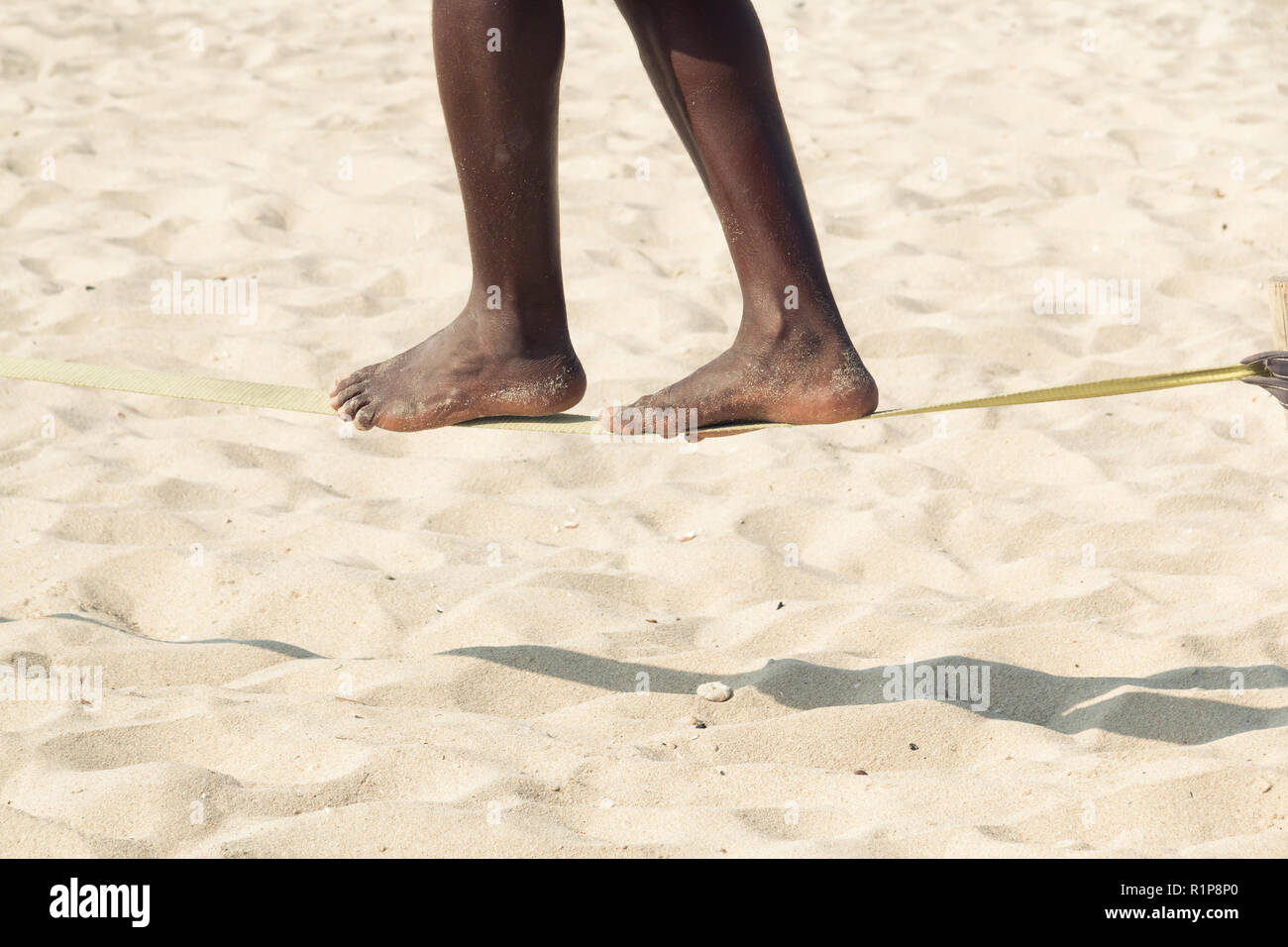 Afro-american guy practising slack line on the beach. Slacklining is a practice in balance that typically uses nylon or polyester webbing tensioned be Stock Photo
