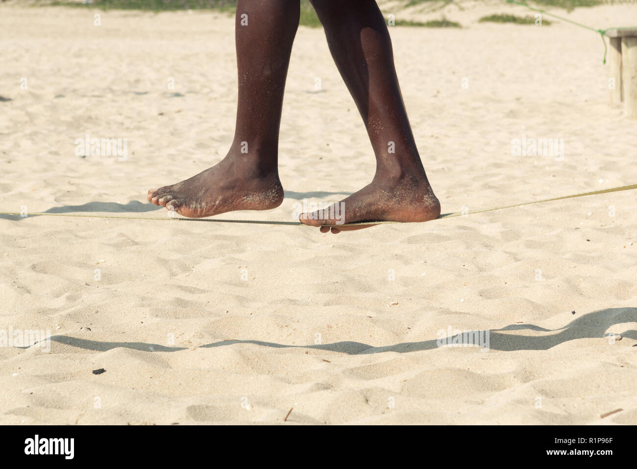 Closeup afro-american man feet walking on tightrope or slackline on sandy background. Slacklining is a practice in balance that uses nylon or polyeste Stock Photo