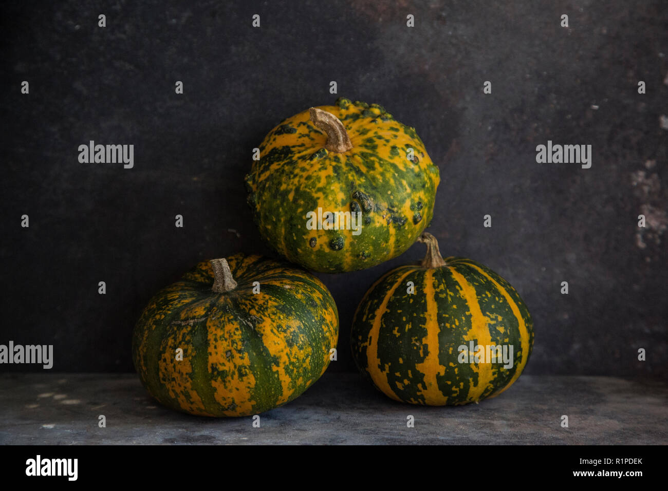 Three small squashes on a textured grey background with quite a dark feel to the image Stock Photo