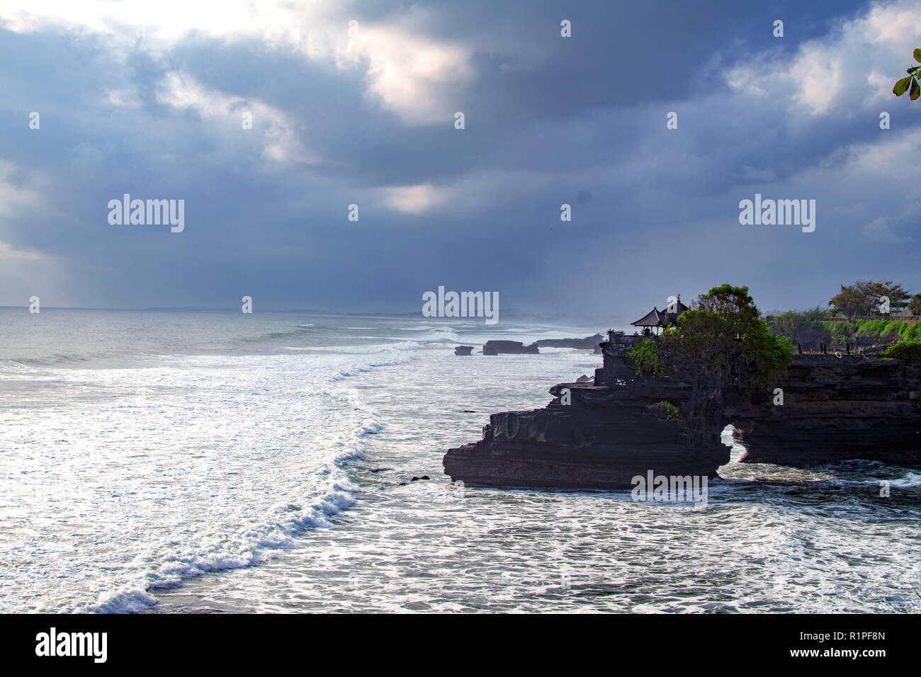 Chimeric temple on the water. Water temple in Bali. Indonesia nature landscape. Famous Bali landmark. Splashing waves and stone. Cloudy day in Indonesia. Water and rocks before storm Stock Photo