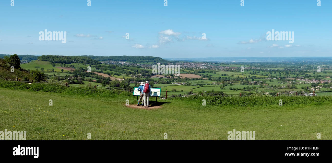 Nympsfield, Gloucestershire, UK - 24th May 2016: Two people discuss the view by the information signboard at Coaley Peak viewpoint. The view over The Severn Vale from the Cotswold escarpment near Nympsfield is one of many extensive panorams to be seen from the Cotswold Way long distance footpath. Stock Photo