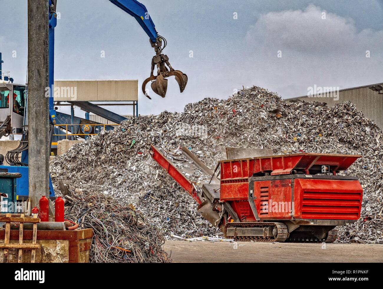 A grab crane lifting large amounts of scrap metal into a machine which reduces the sixe of the waste metal for further recycling processes. Stock Photo