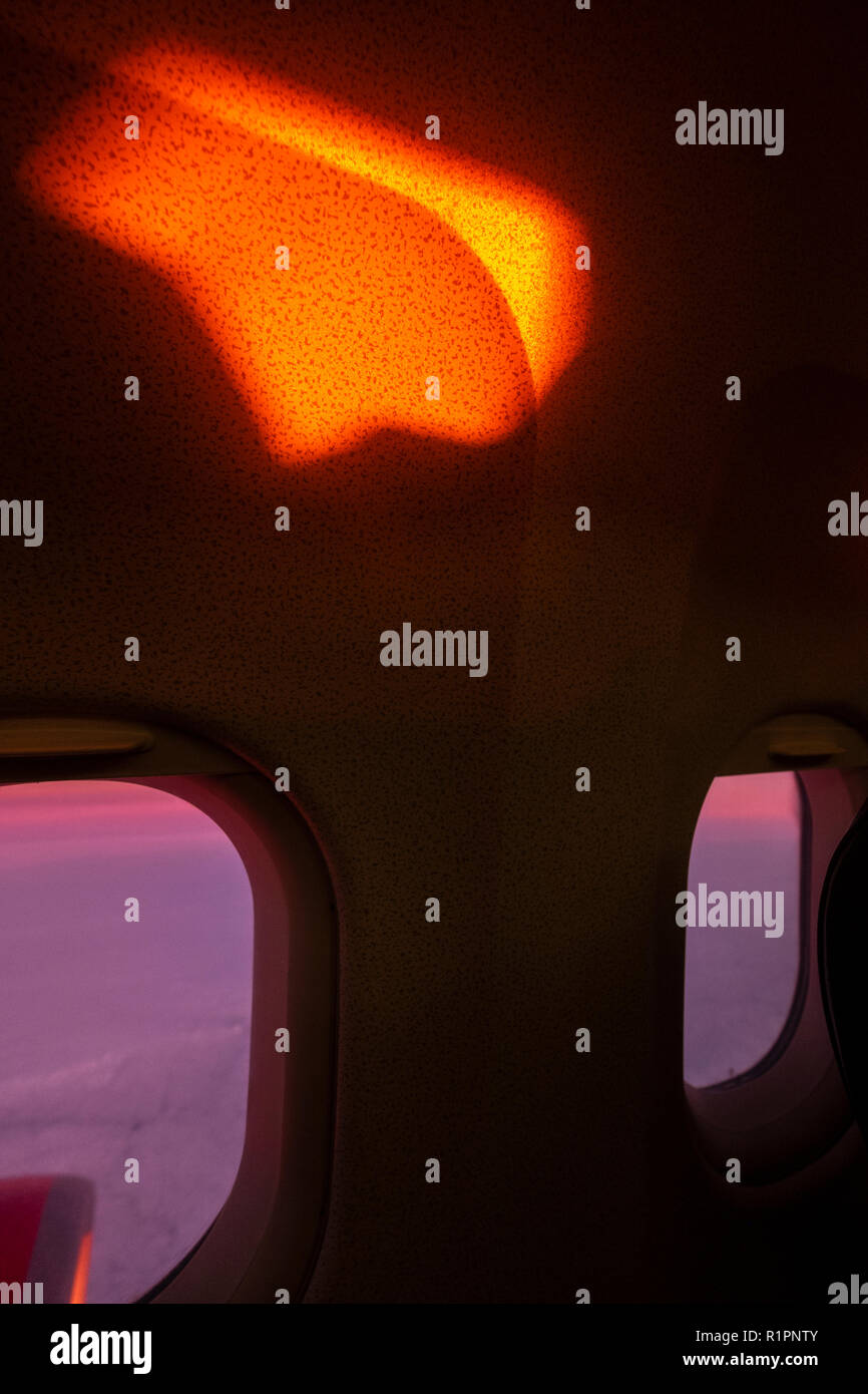 Abstract image with dawn light in deep red on the interior cabin wall and porthole windows overlooking the clouds from an early morning flight. Stock Photo