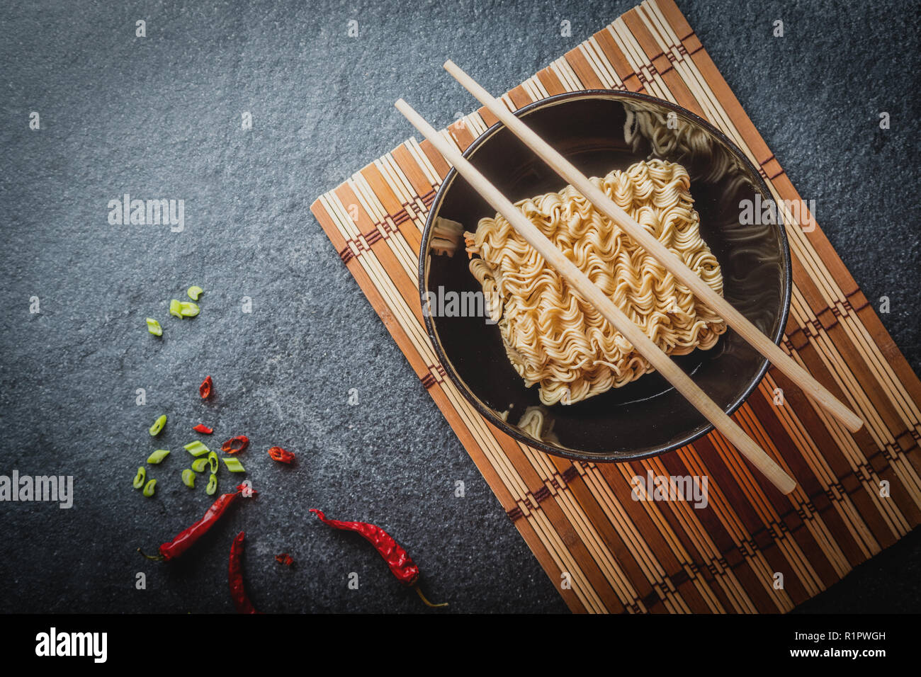 Black bowl of asian instant noodles with and red chili peppers and green onion and chopsticks Stock Photo