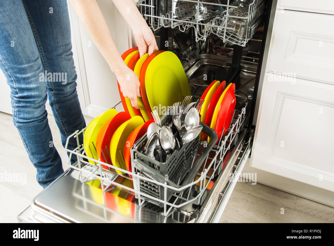 Woman is standing near dishwasher and taking clean plate from it, housework concept Stock Photo