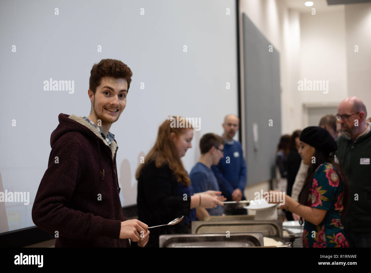 Cheltenham, UK. 14th Nov 2018.. Student volunteer smiling at camera, serving food Credit: Victor Storublev/Alamy Live News Stock Photo