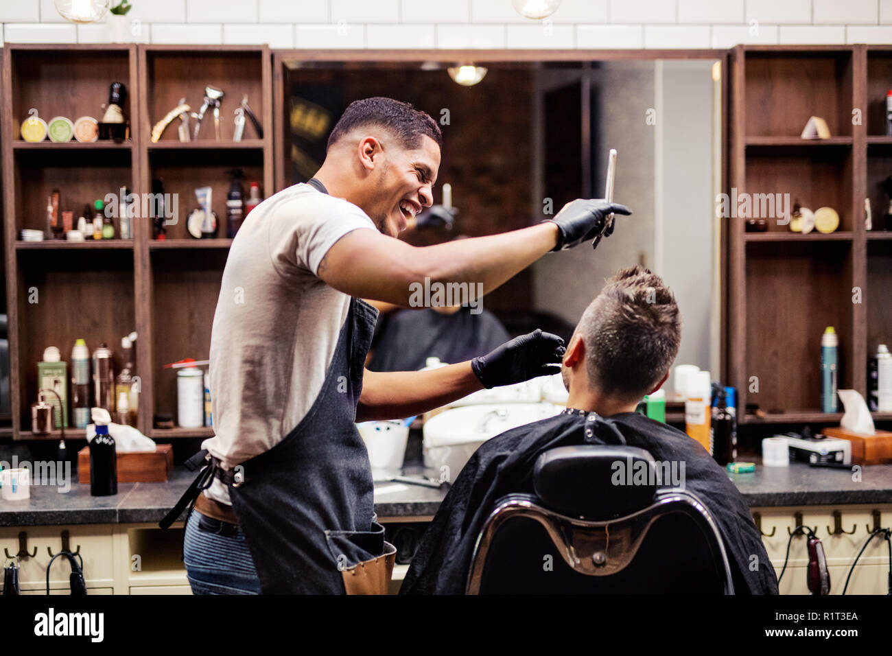 Rear view of man client visiting haidresser and hairstylist in barber shop. Stock Photo