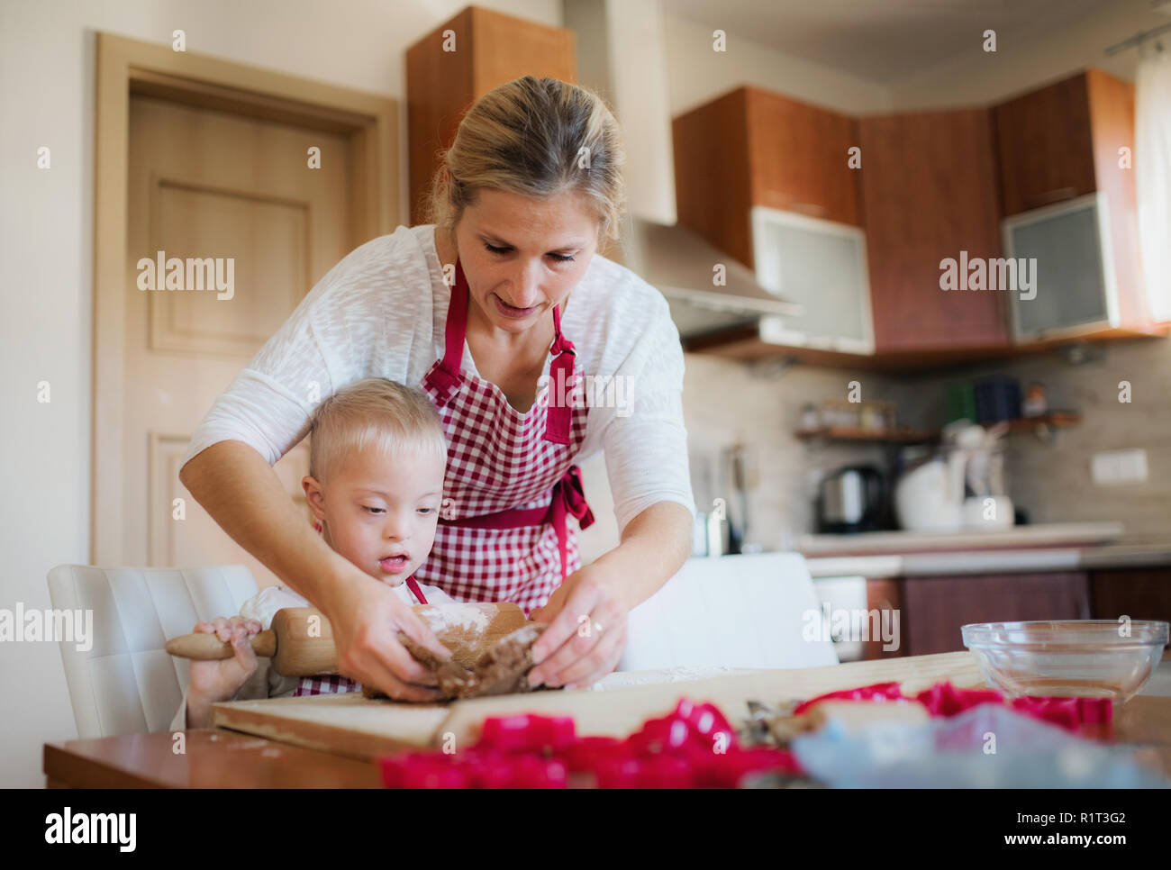 A handicapped down syndrome boy with his mother indoors baking. Stock Photo