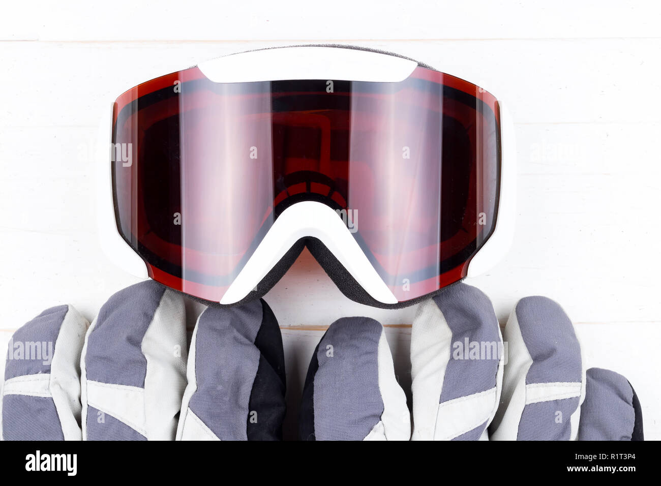 Winter gloves and goggles on white natural wooden table background. Concept of skiing or snowboarding. Flat lay top view. Stock Photo