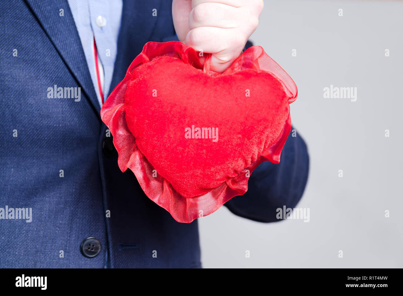 Young elegant man holding red heart on Valentine's Day. Blue suit. Copy ...