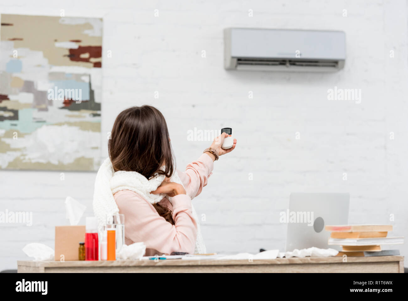 sick young woman sitting at workplace and pointing at air conditioner