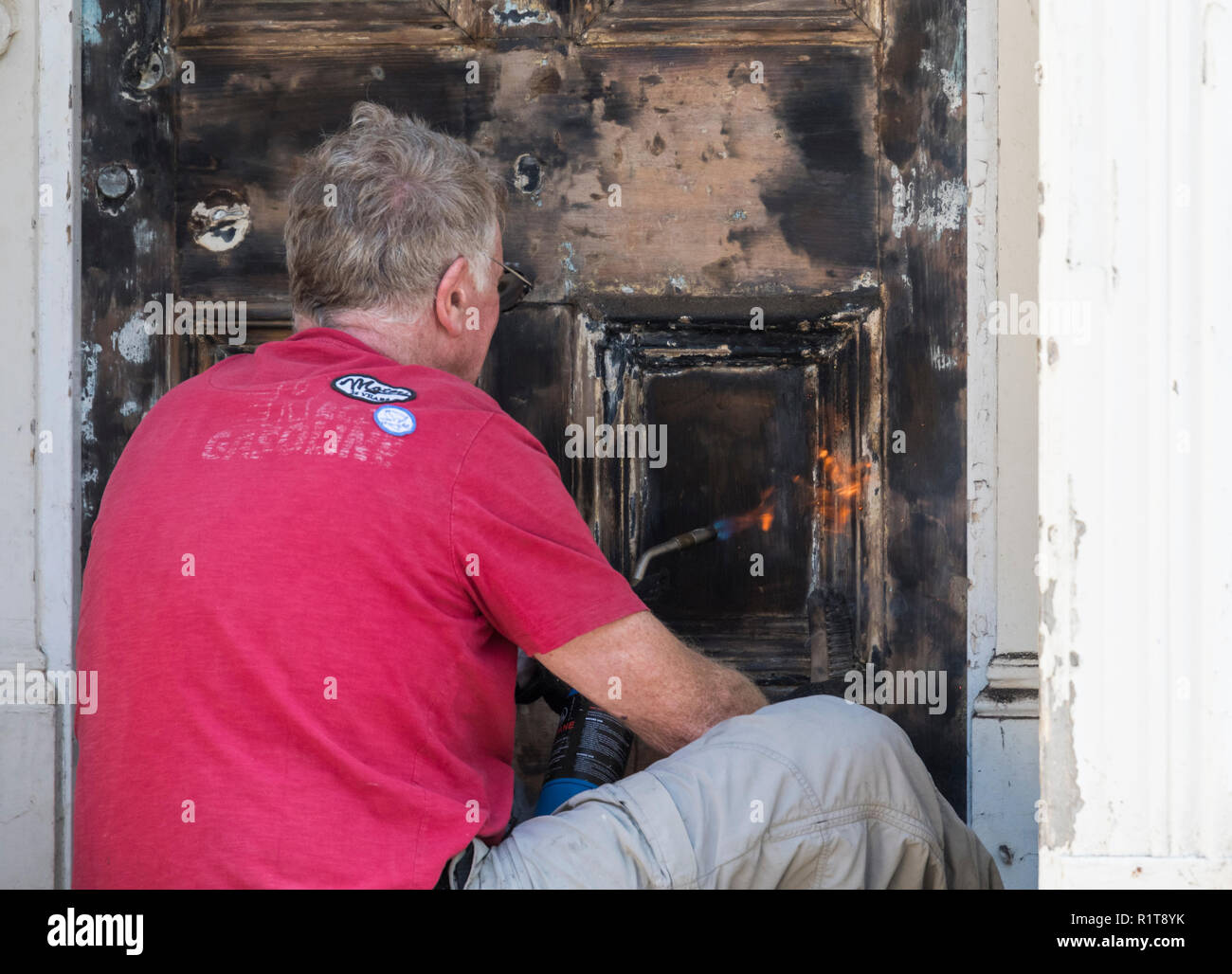 Man using hot gas powered blow torch (blowtorch) to strip paint from a front door. House renovations, painter & decorator. Stock Photo