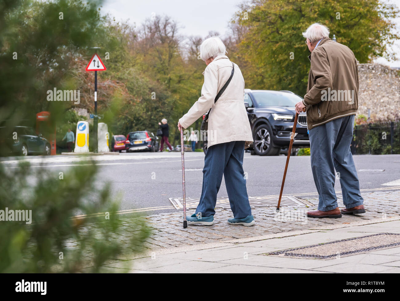 Senior couple of people with walking sticks crossing a road in the UK. Stock Photo