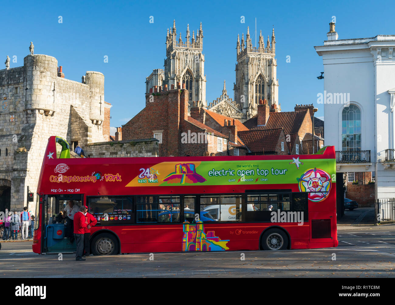 An electric open topped tourist bus parked in St Leonards Place in York city centre, with Bootham Bar and York Minster in the background, North Yorksh Stock Photo