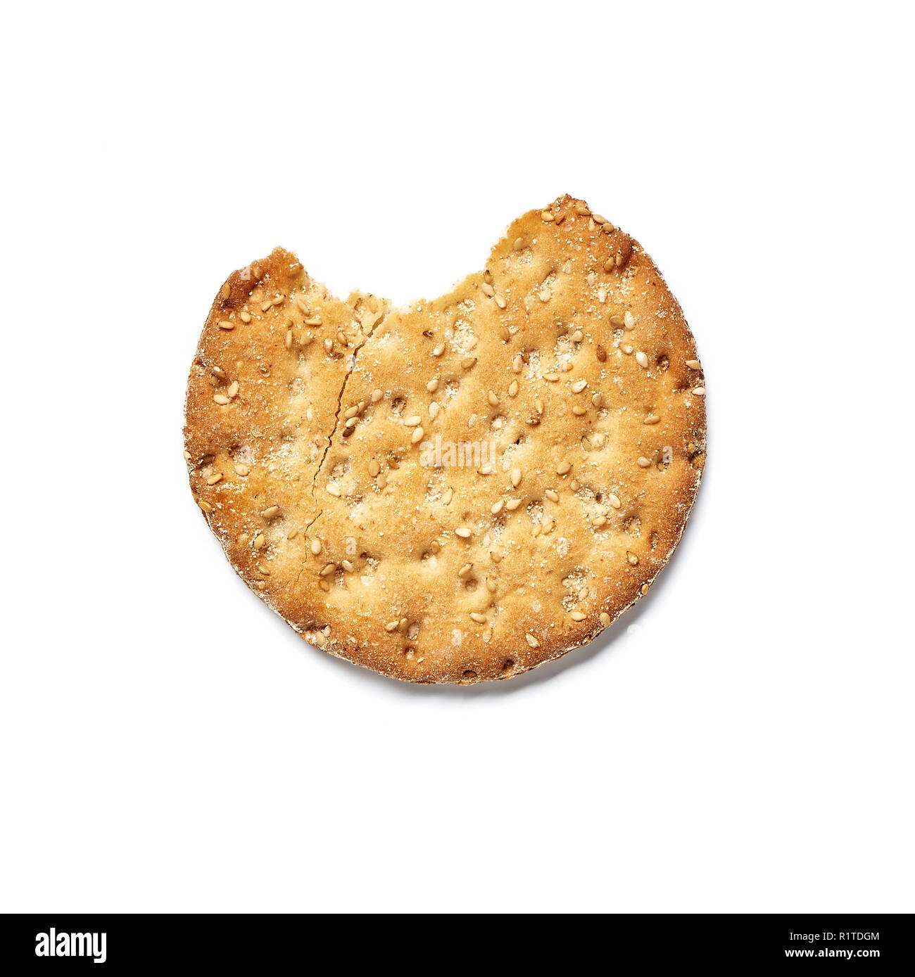 A bite of a round wheat cracker with sesame isolated on white ...