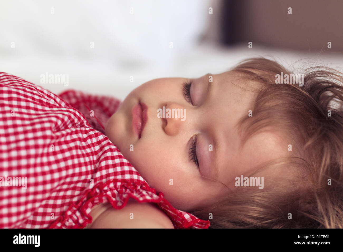 Close up portrait of a beautiful nine month old baby girl sleeping on blurred background. Sleeping child face. Cute infant kid. Child portrait in past Stock Photo