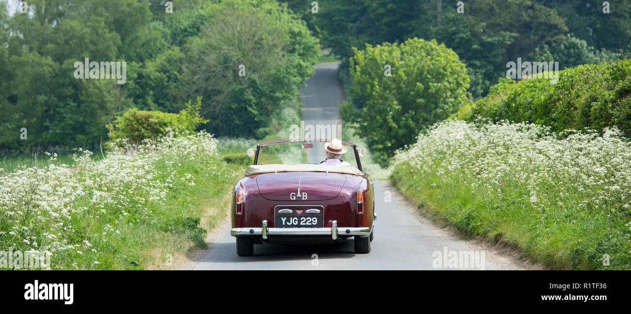 Motorist driving away in a British made Alvis TD21 classic car along a country lane in The Cotswolds, England Stock Photo