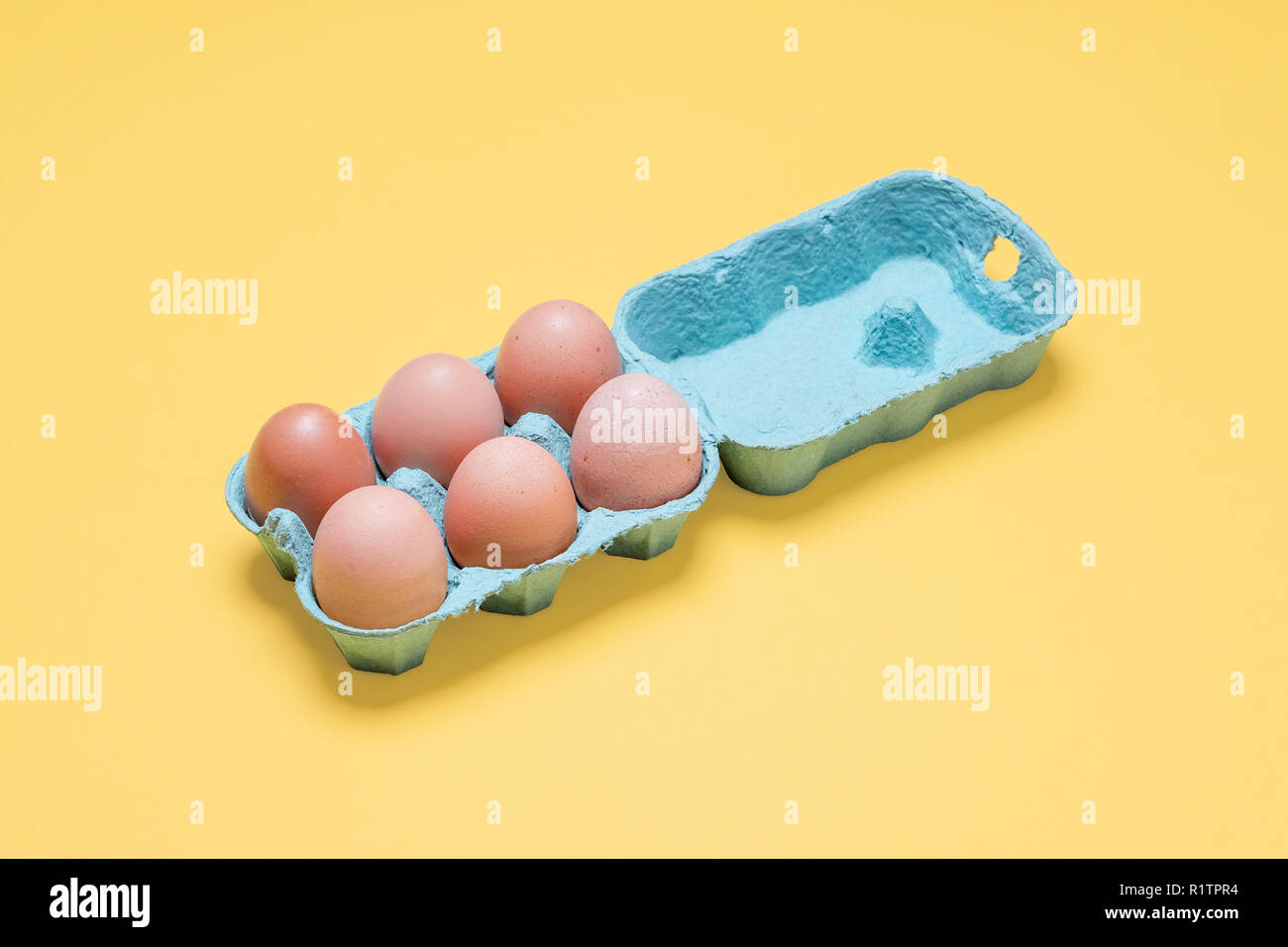 Half dozen free range organic brown eggs in carton.  Six brown eggs in crate container on a bright pastel yellow background Stock Photo