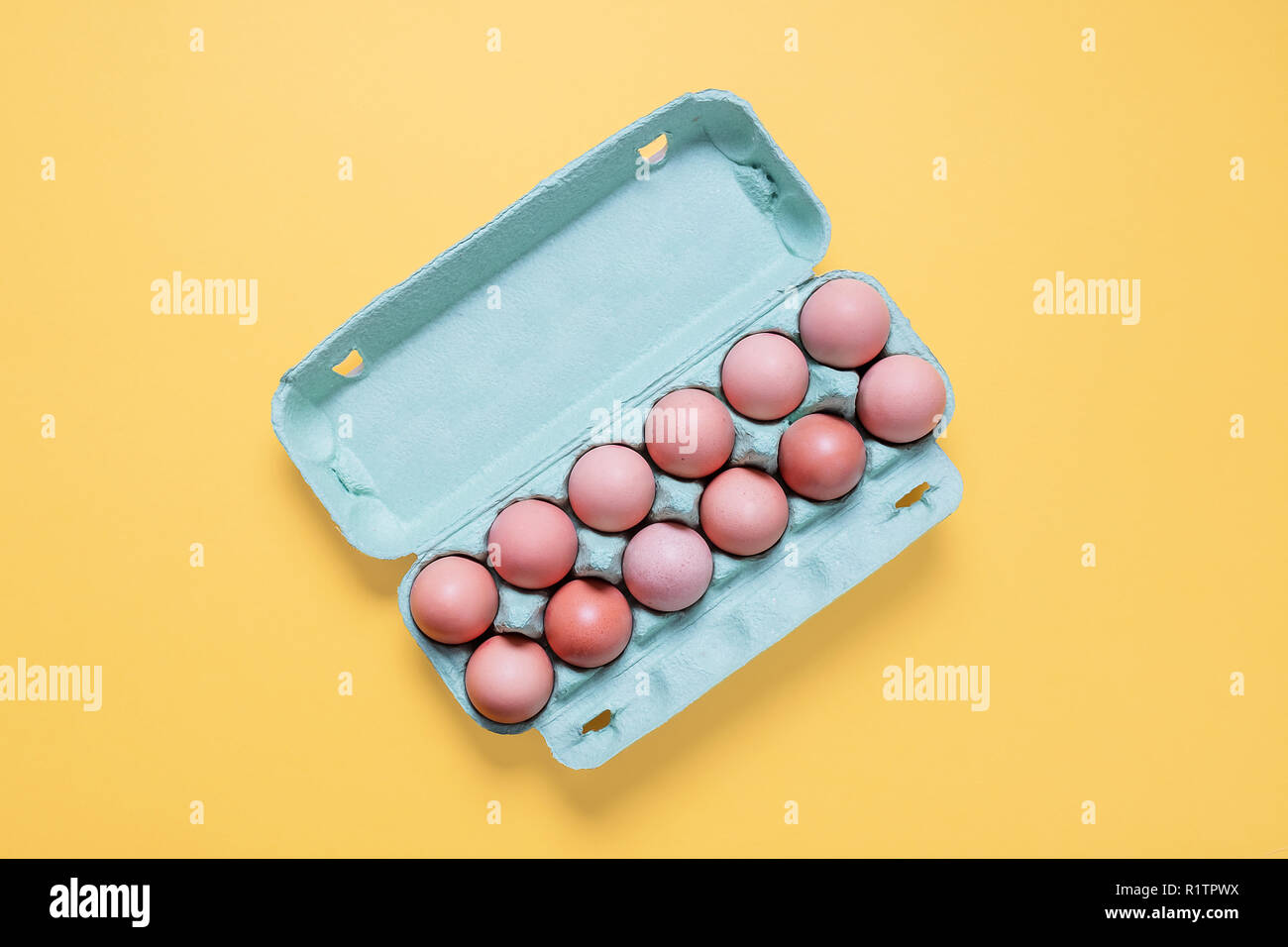 Top view of dozen free range brown eggs in carton.  Twelve brown eggs in crate container on a bright pastel yellow background Stock Photo