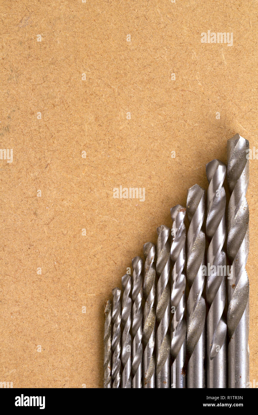 Well used and rust specked twist drill bits on an old MDF board with copy space Stock Photo