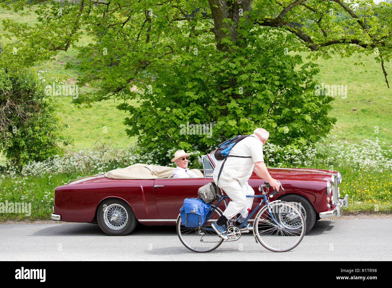 Driver in Alvis classic car chats with cyclist along a country lane in The Cotswolds, England Stock Photo