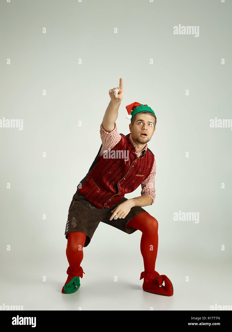 The happy smiling friendly man dressed like a funny gnome or elf pointing up on an isolated gray studio background. The winter, holiday, christmas concept Stock Photo