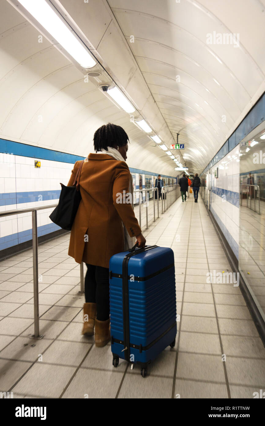 Tube commuters time, young woman pushes suitcase along underground tube corridor Stock Photo
