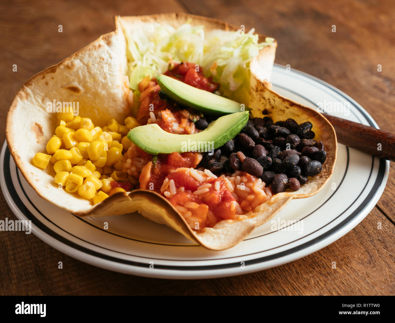 Mexican taco bowl with lettuce, corn, Mexican spicy, tomato rice, black beans, salsa and avocado on a flour tortilla. Stock Photo