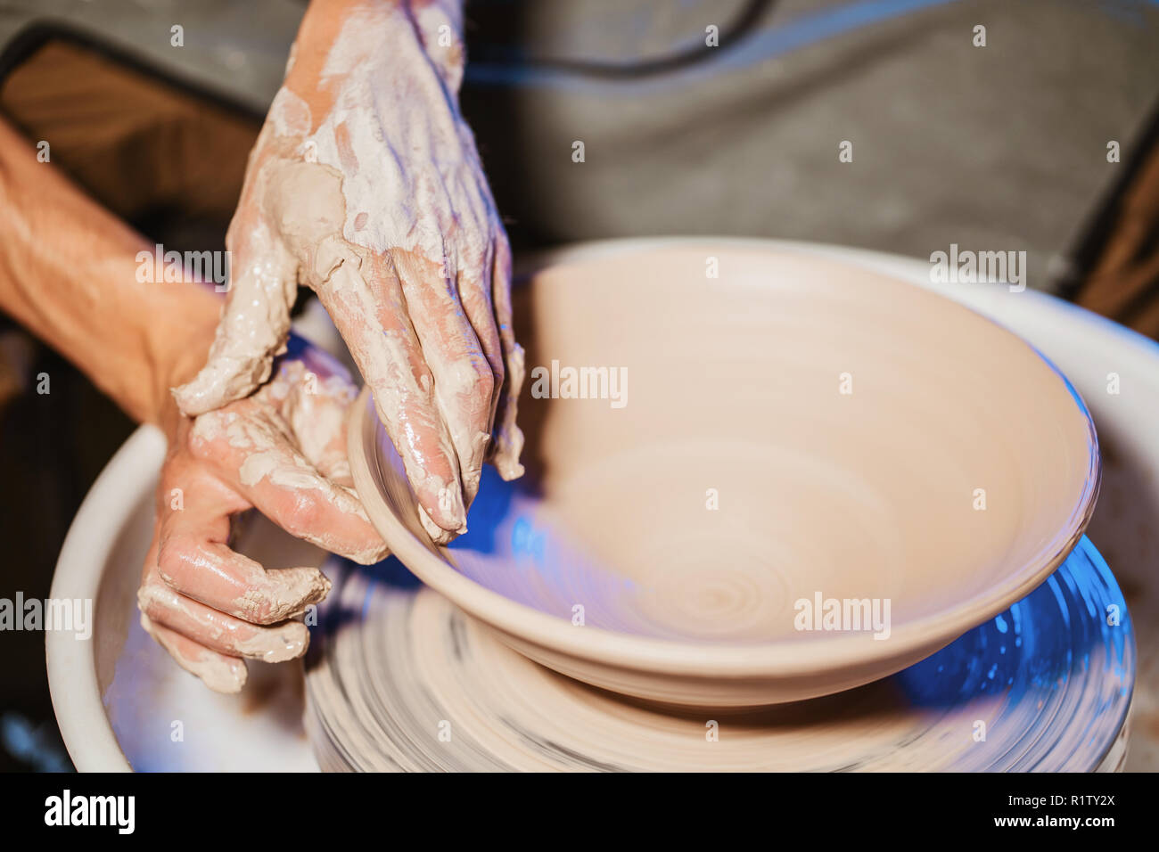 Experienced potter shapes the clay product plate with pottery tools