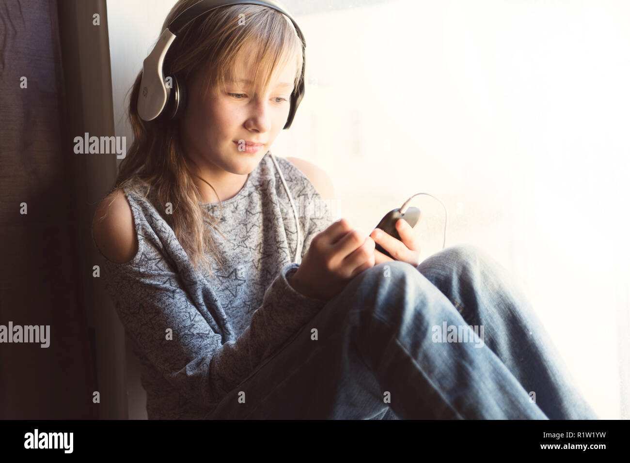 A young 10 years woman listening music close to the window Stock Photo