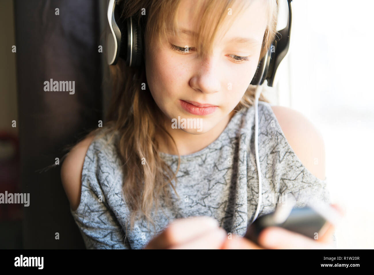 A young 10 years woman listening music close to the window Stock Photo