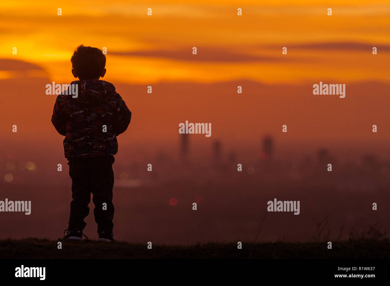 A four year old boy looks over Manchester City Centre in the distance at sunset taken from the Pennine village of Mossley on Wednesday 14th November 2 Stock Photo
