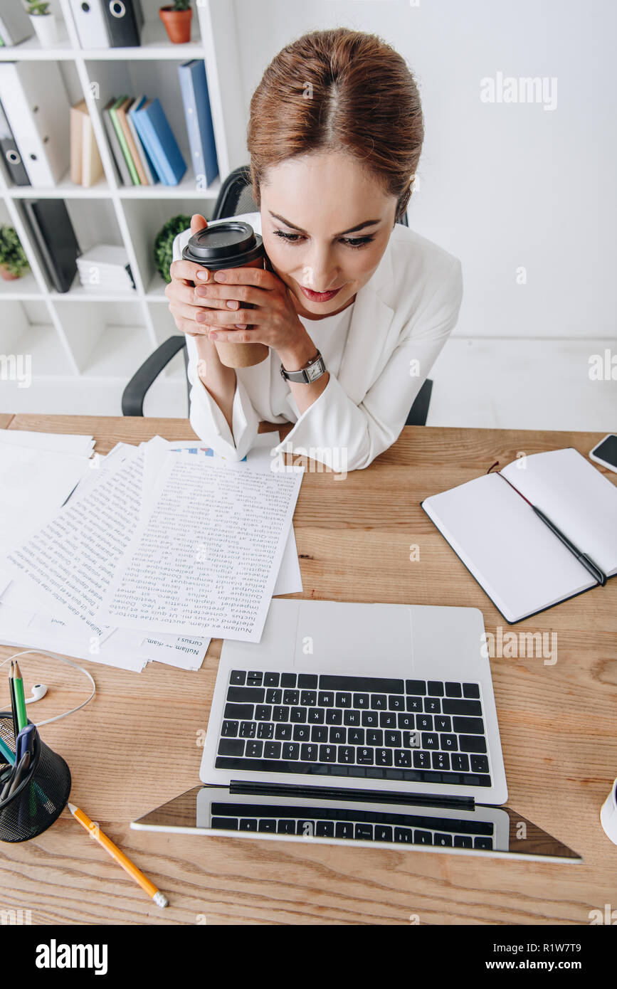 overhead view of businesswoman with coffee to go working with documents ...