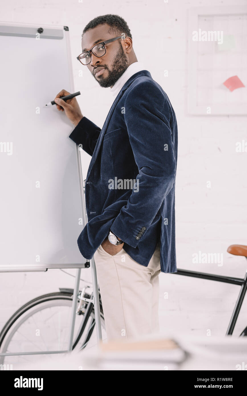 bearded african american businessman in velvet jacket writing on whiteboard in office with bicycle Stock Photo