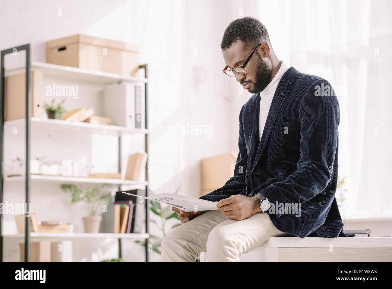 stylish african american businessman in velvet jacket reading newspaper in office Stock Photo