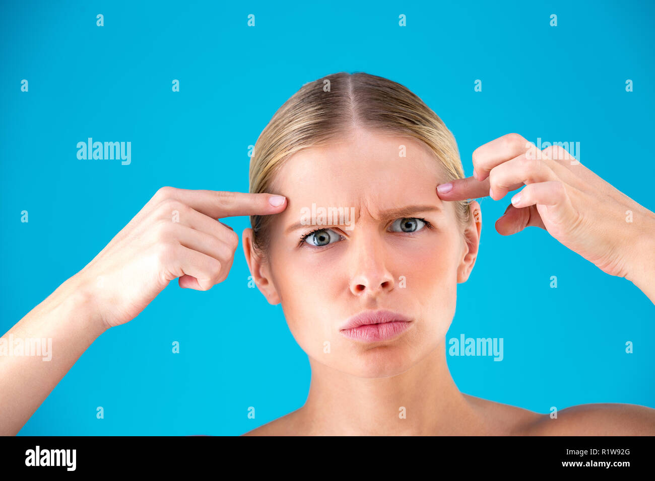 Young Woman checking her wrinkles on her forehead - isolated on blue Stock Photo