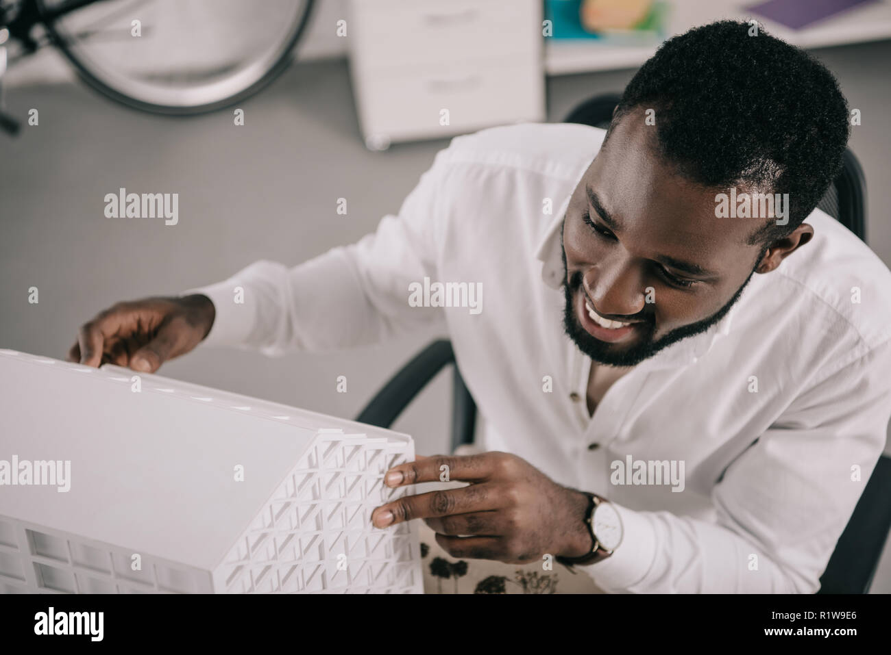 high angle view of smiling handsome african american architect looking at architecture model in office Stock Photo