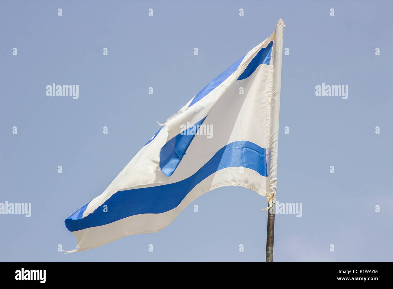 A tattered Israeli Flage aloft in a stiff breeze against a blue sky at the Banais Nature Reserve in the Golan Heights Israel. Stock Photo