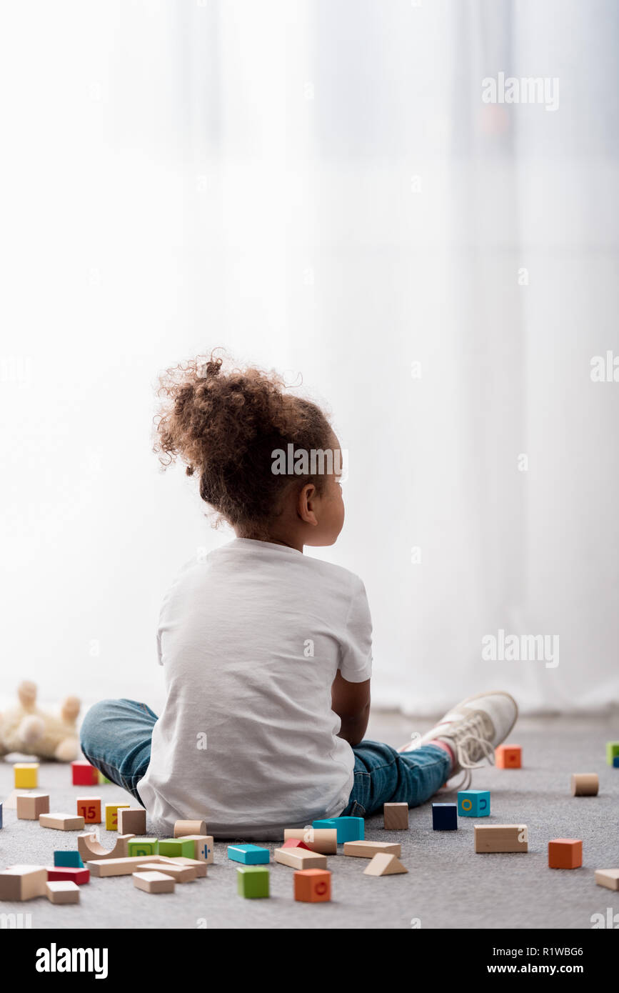 Back view of little child in white t-shirts surrounded by colourful toy ...