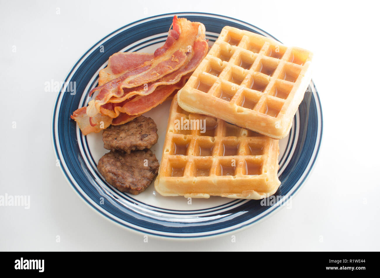 Plate of waffles with maple syrup, sausage patties and bacon strips Stock Photo
