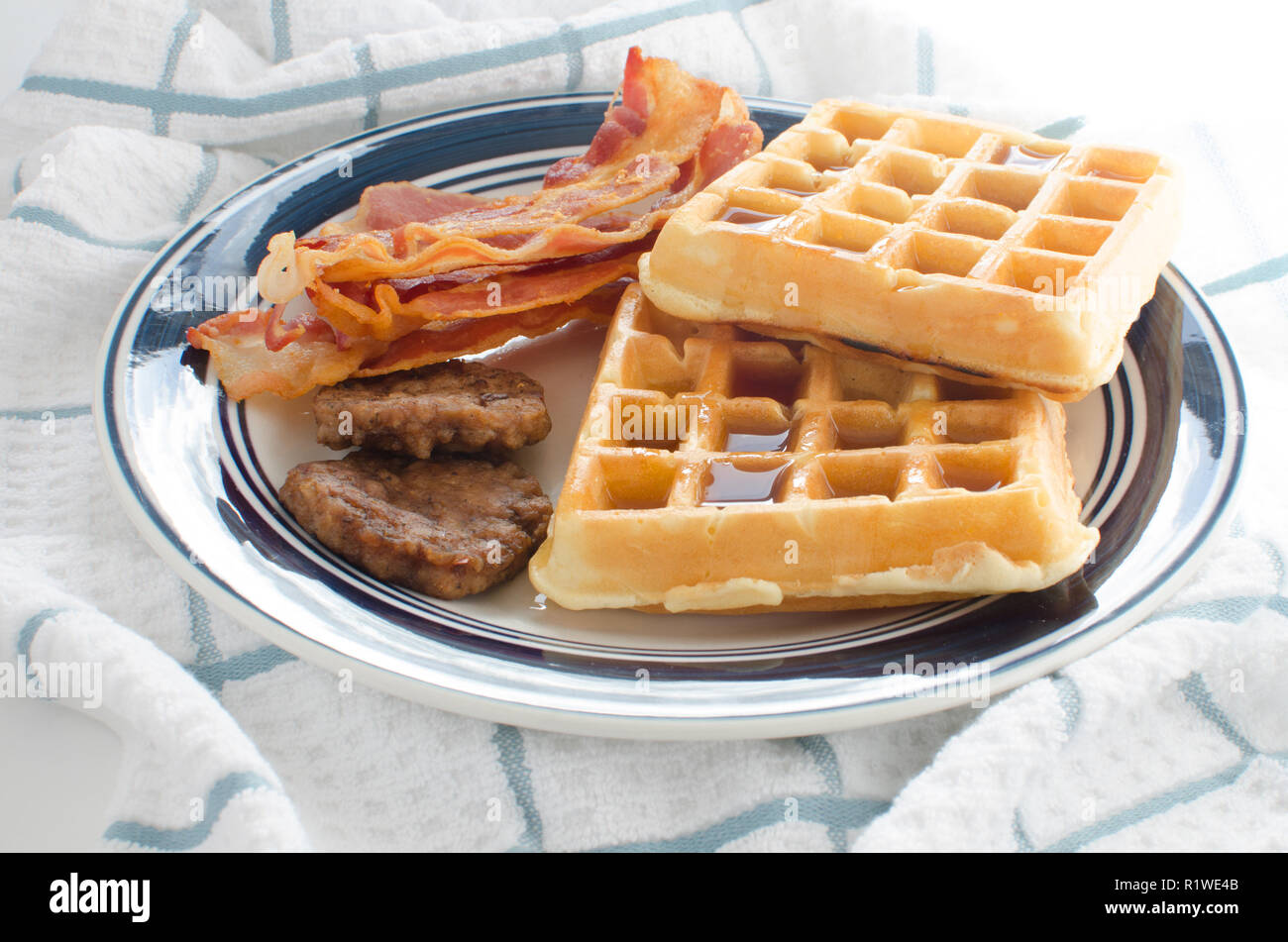 Plate of waffles with maple syrup, bacon strips and sausage patties