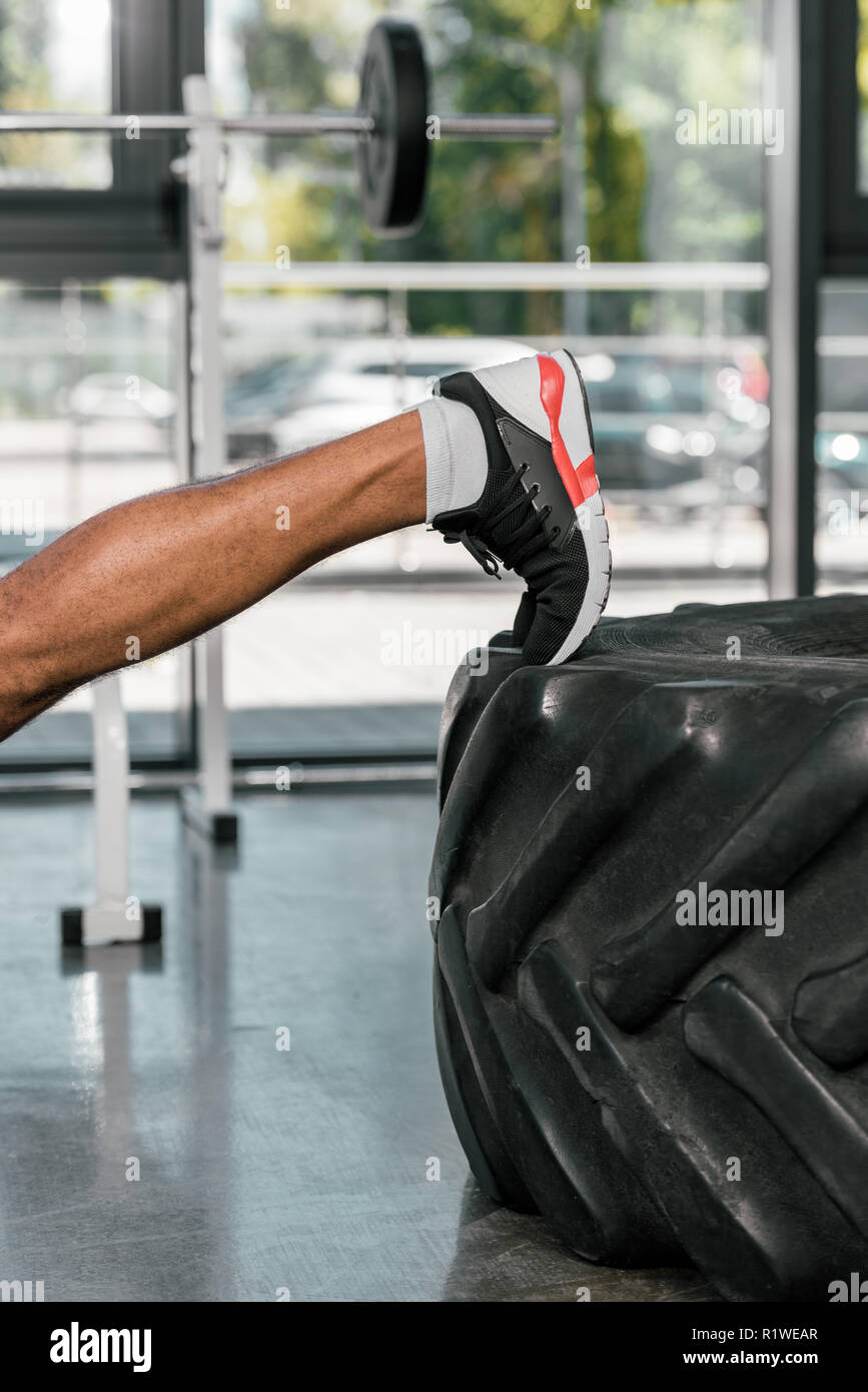 cropped shot of muscular male leg on tire in gym Stock Photo